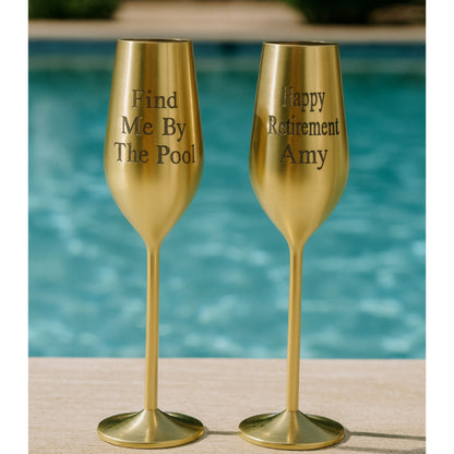 Two gold champagne flutes with engraved text by a pool.