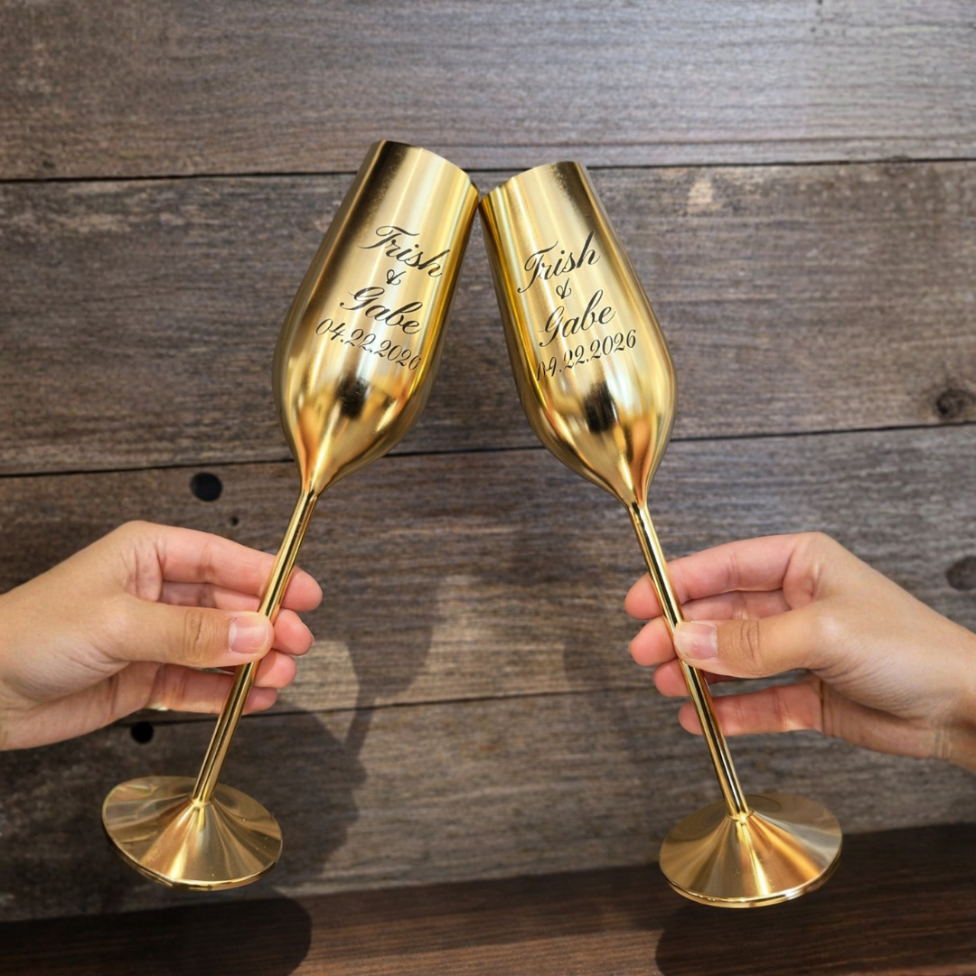 Two gold champagne flutes being held against a wooden background