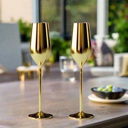 Two gold champagne flutes on a table with a blurred outdoor background