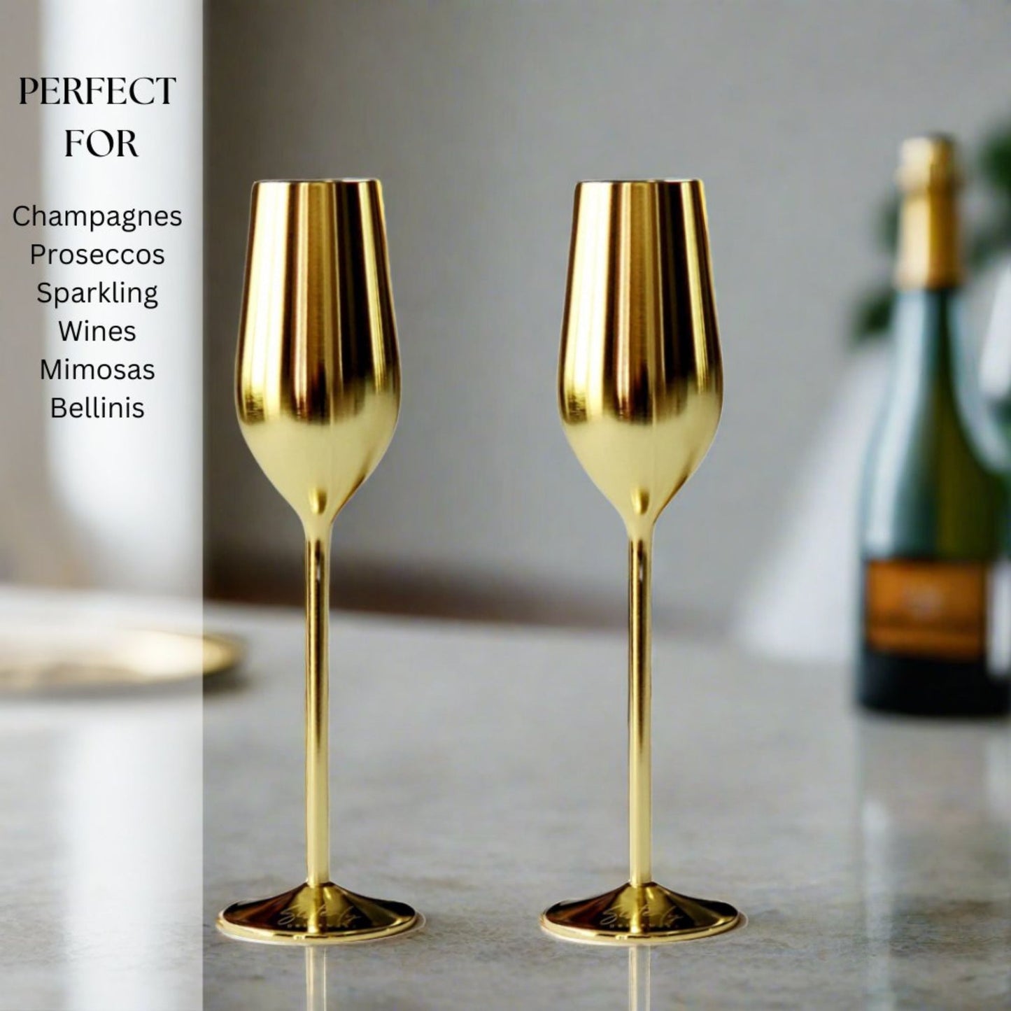 Two gold champagne flutes on a marble surface with a blurred bottle in the background.