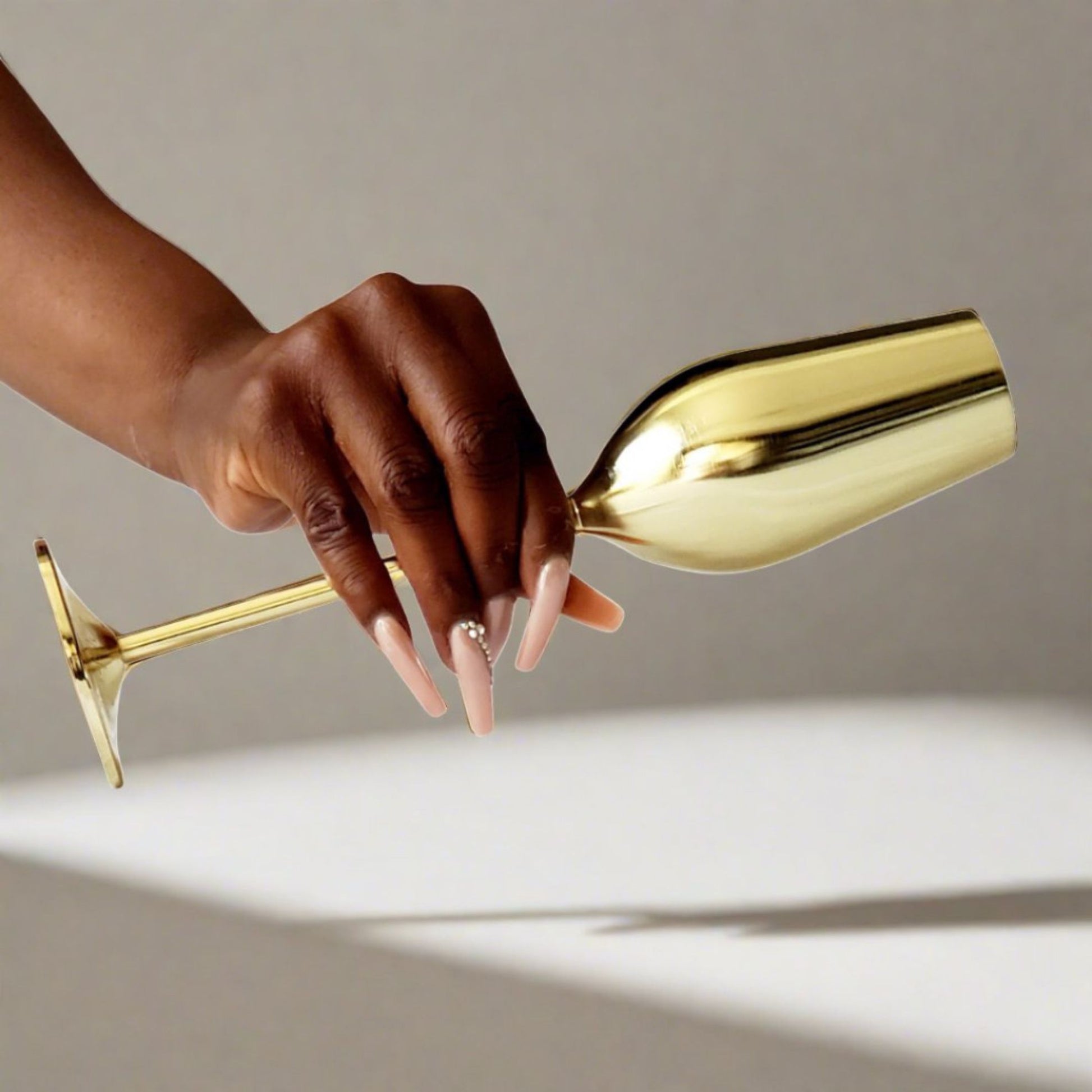 Hand holding a gold wine glass against a neutral background