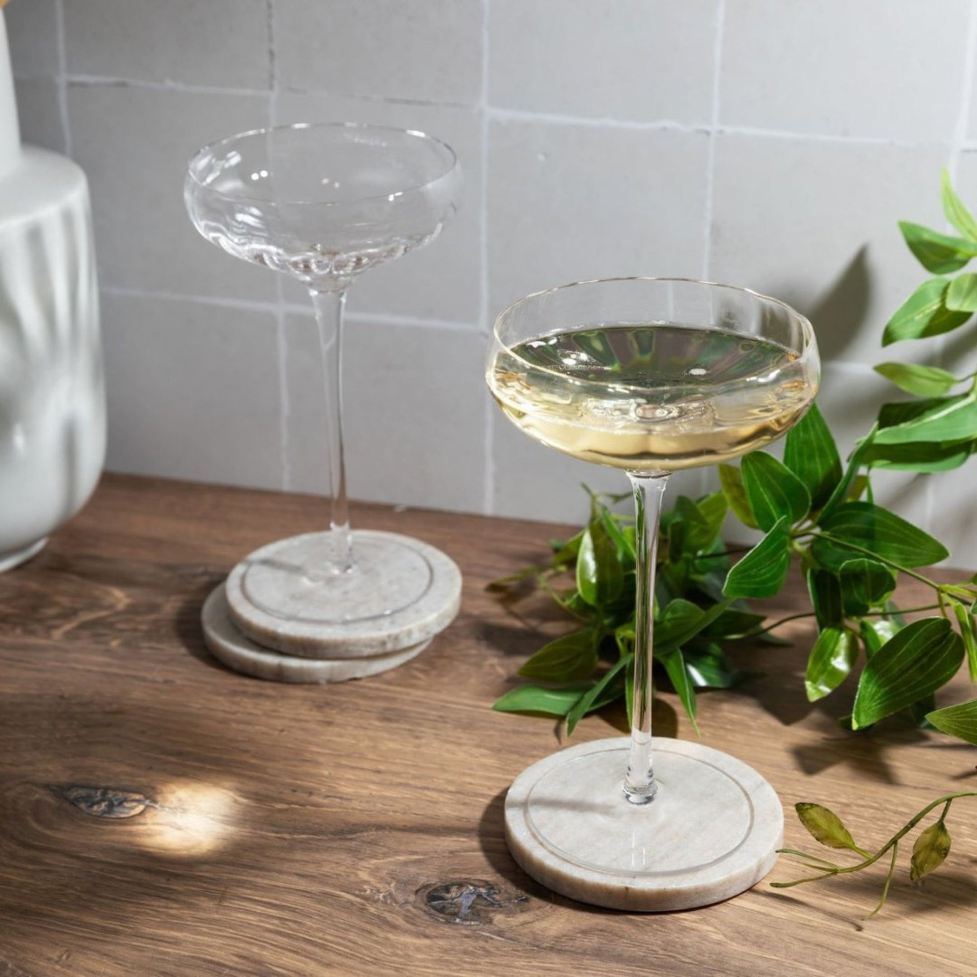 Two coupe glasses with champagne on a wooden surface with a plant in the background