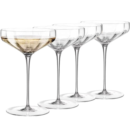 Set of four clear cocktail glasses with one containing a light-colored liquid on a white background