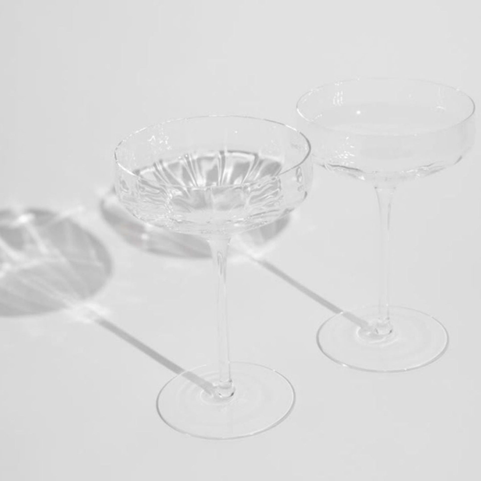 Clear coupe glass cocktail glasses on a light gray background