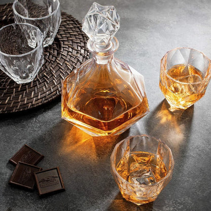 Glass decanter and glasses with whiskey on a dark surface with chocolate bars.