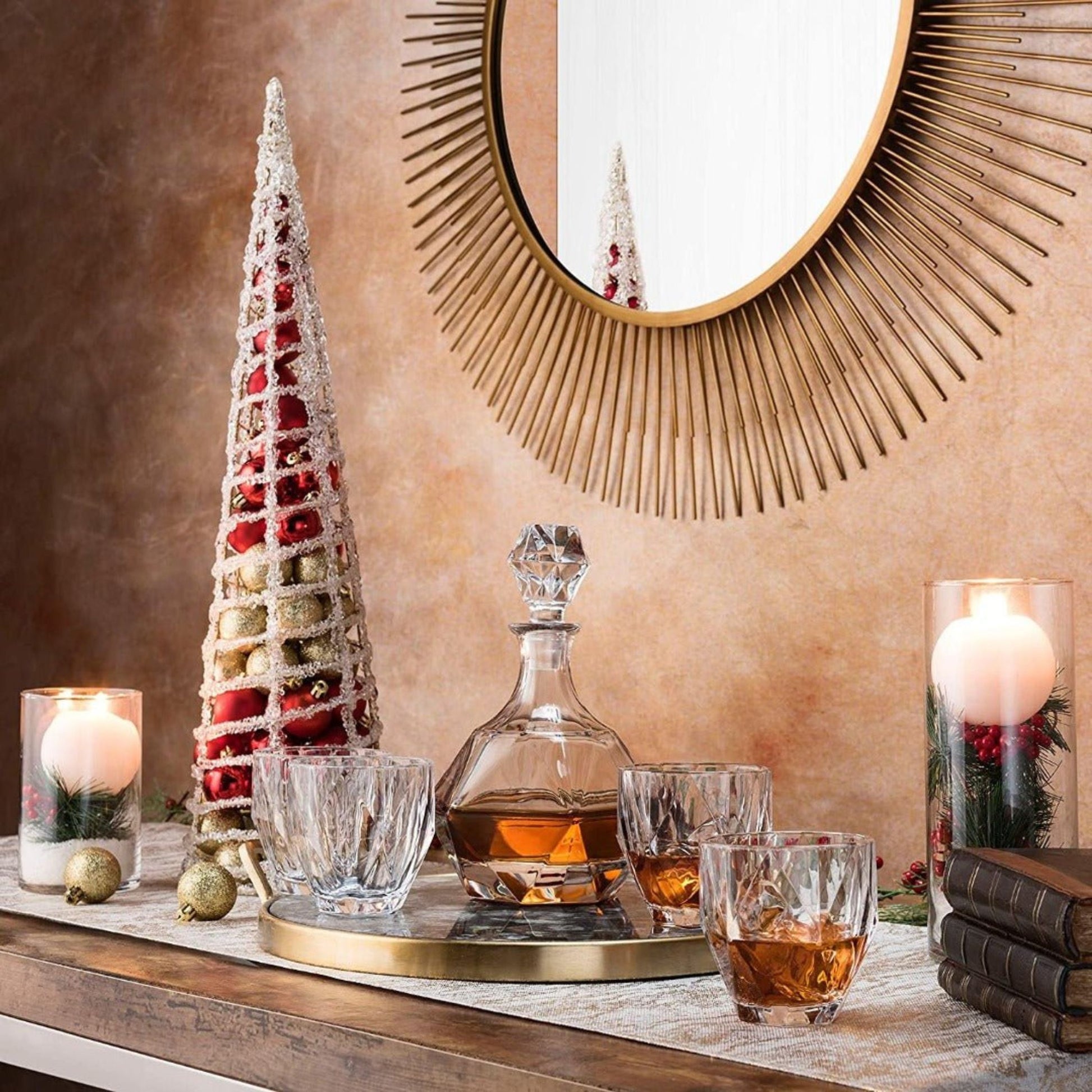 Decorative table setting with a decanter, glasses, and Christmas tree on a wooden surface.