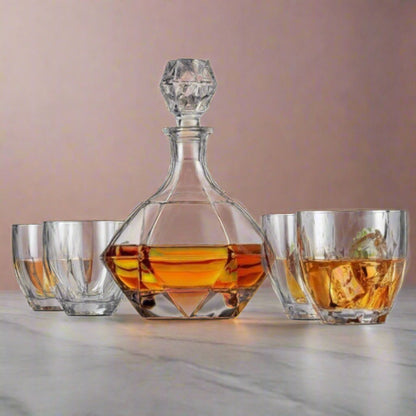 Crystal decanter with geometric design filled with amber liquid, accompanied by three glasses on a light surface.