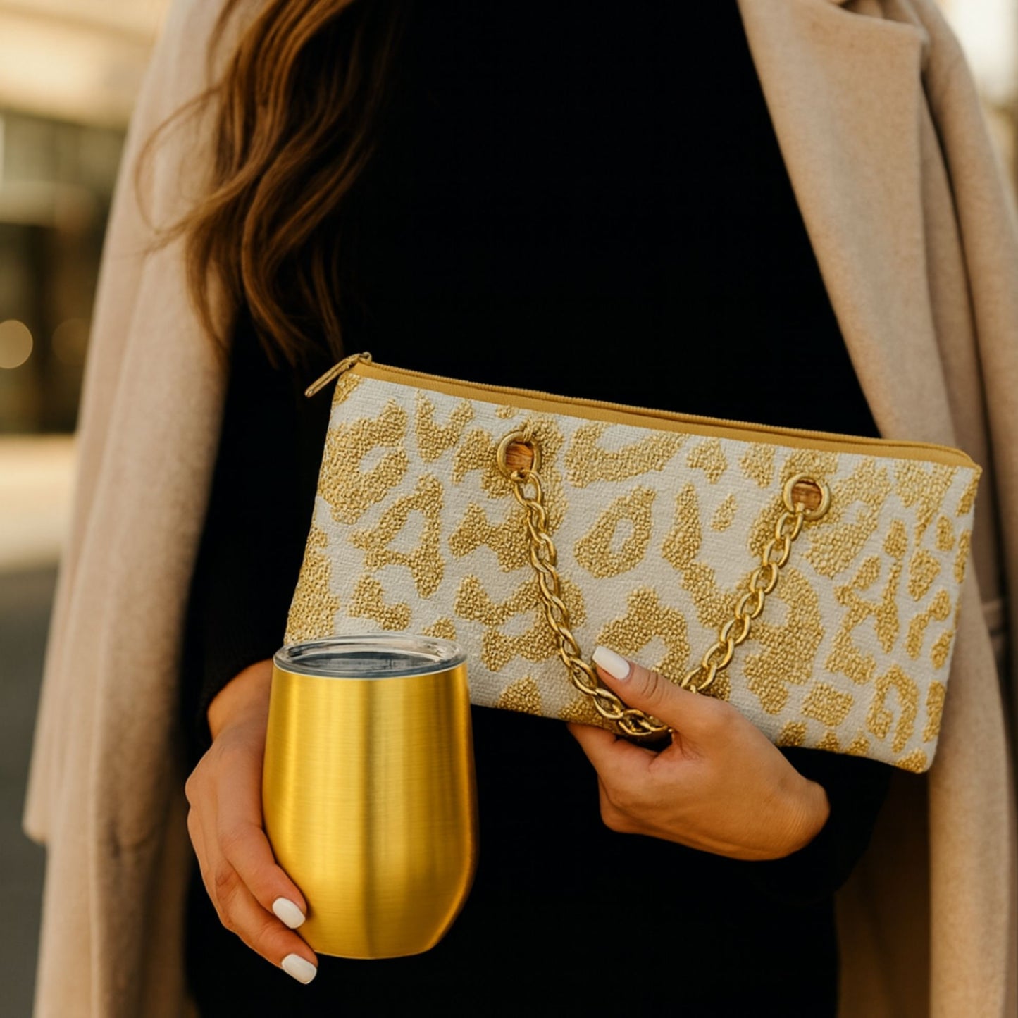 Person holding a gold clutch with a chain strap and a gold cup.
