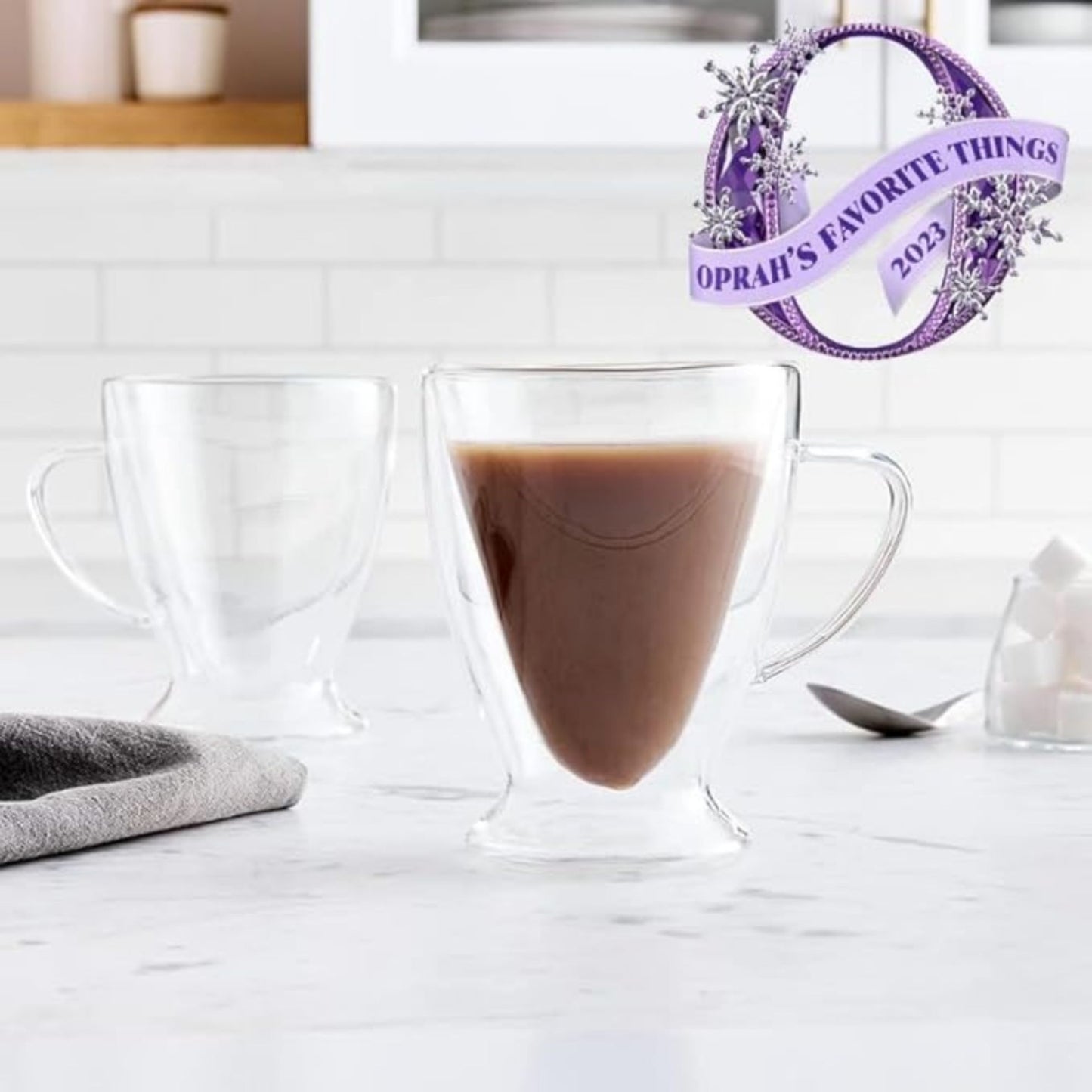 Clear glass mug with hot chocolate on a white surface, featuring Oprah's Favorite Things 2023 logo.