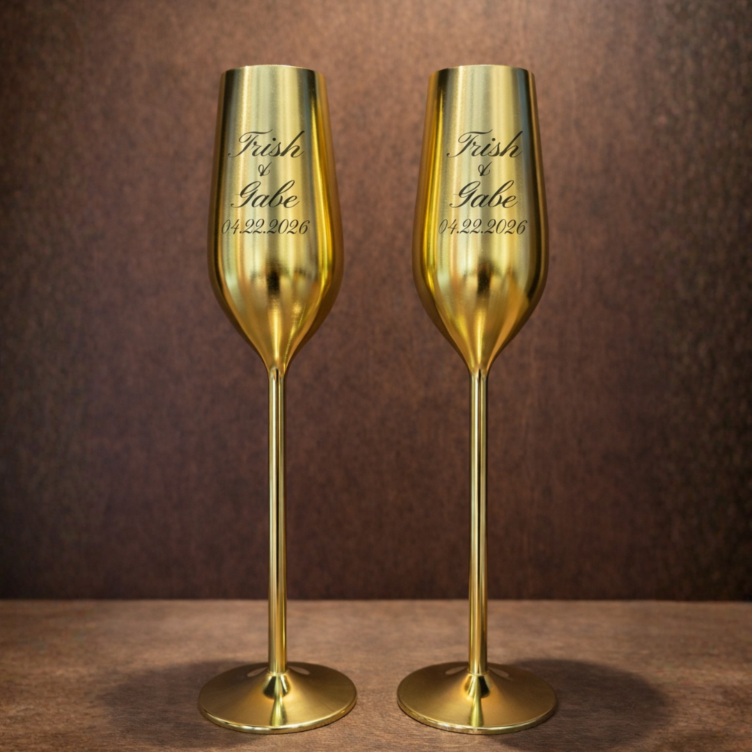 Two gold champagne flutes with engraved text on a brown background