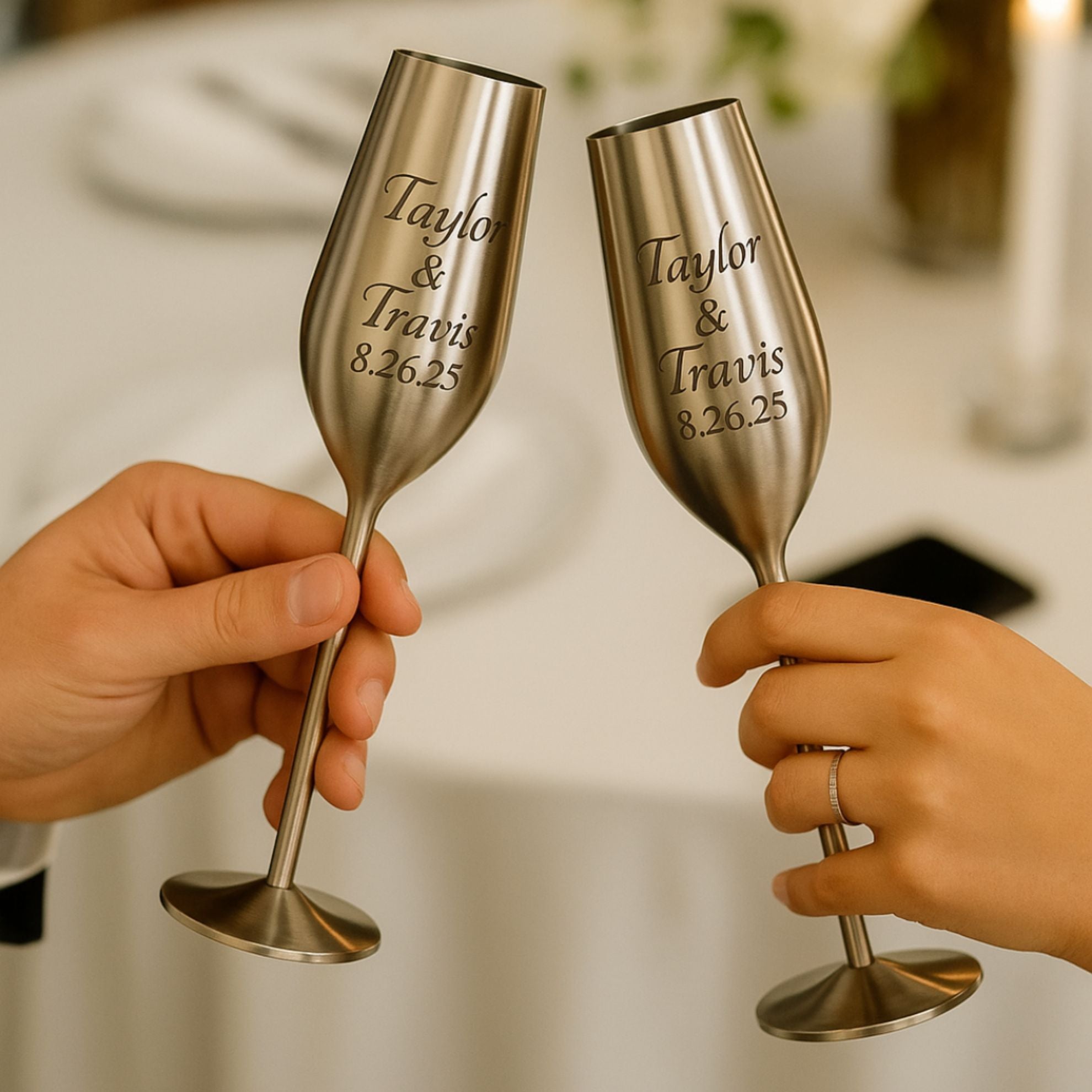 Two silver champagne flutes with engraved names and date, held by two hands against a blurred background.