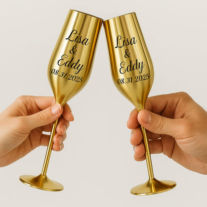 Two gold champagne flutes held by hands with engraved names and date on a light background