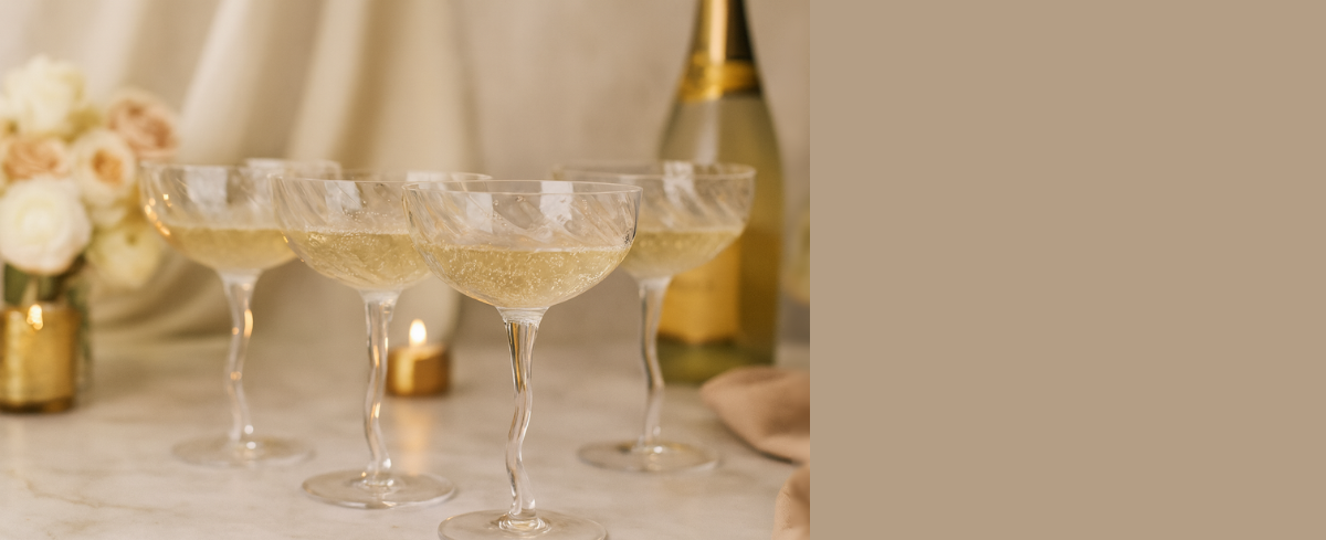 Three champagne glasses with a bottle of champagne on a beige background
